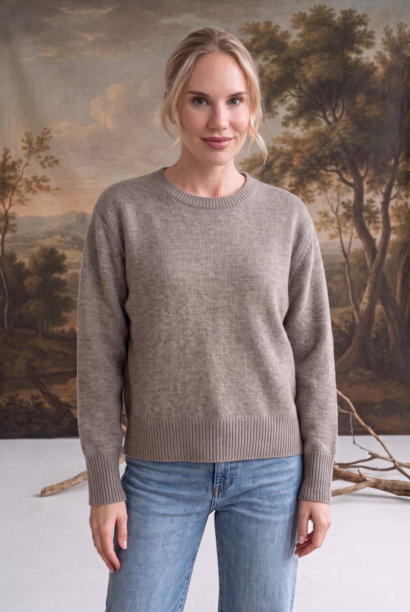 Woman wearing a graced taupe crew neck sweater with ribbed cuffs and hem, styled with blue jeans.