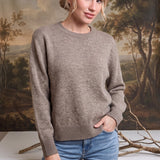 Woman wearing a graced taupe crew neck sweater with ribbed cuffs and hem paired with blue jeans