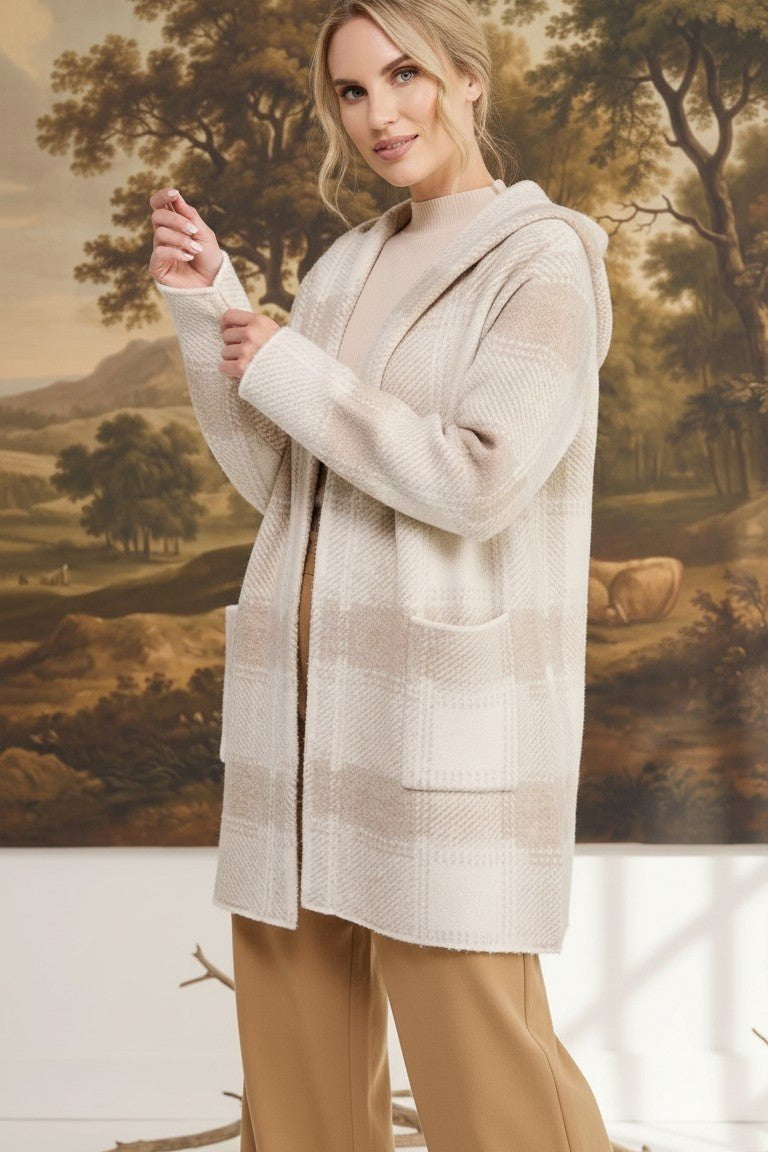 Model wearing a graced beige plaid hooded sweater cardigan with front pockets over a neutral top and tan trousers.