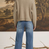 Back view of a woman wearing the graced Dolly zip up sweater jacket in taupe over a denim shirt and blue jeans.