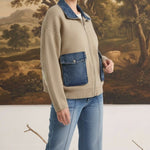 Model wearing graced taupe zip-up sweater jacket with denim collar and pocket details against a landscape backdrop.