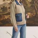 Model wearing graced taupe zip-up sweater jacket with denim collar and pocket details against a landscape backdrop.