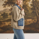 A model wearing a graced taupe zip-up sweater jacket with denim collar and pocket details against a landscape painting.