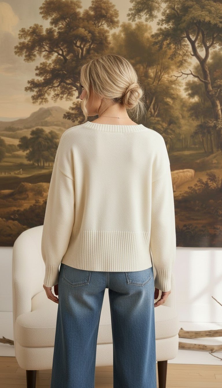 Back view of a woman wearing a graced ivory crew neck sweater with dropped shoulders and wide ribbed hem and cuffs.