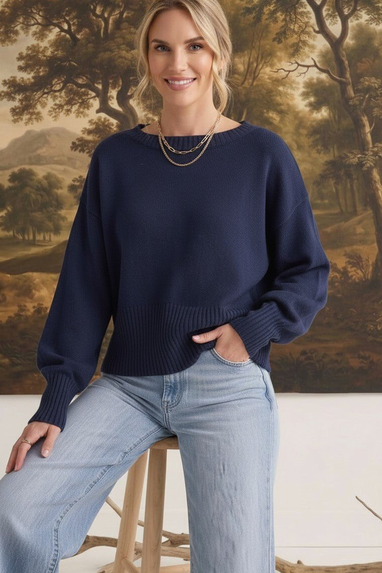 Model wearing a navy graced Eloise crew neck sweater with dropped shoulders and wide ribbed cuffs, paired with jeans.