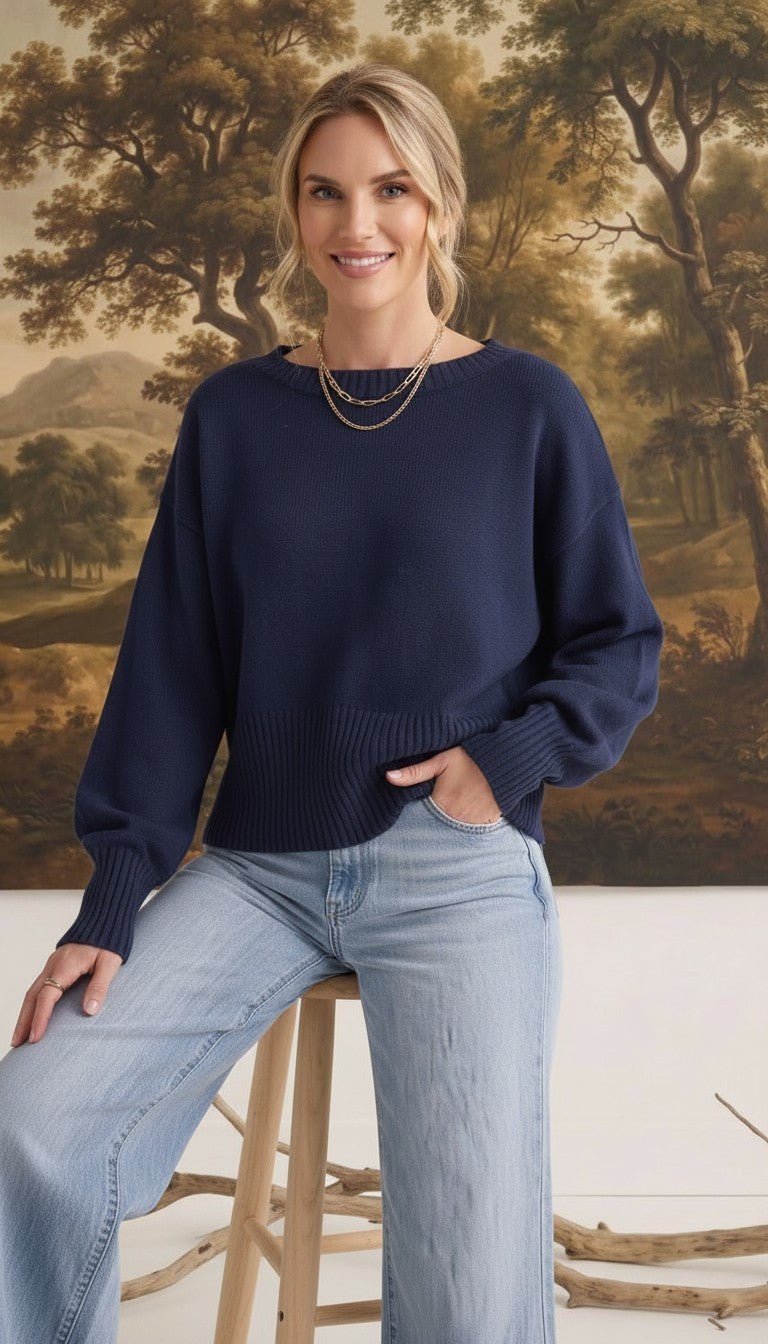 Model wearing a navy graced Eloise crew neck sweater with dropped shoulders and wide ribbed cuffs, paired with jeans.