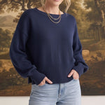 A woman wearing a navy graced Eloise crew neck sweater with dropped shoulders and wide ribbed hem, paired with jeans.