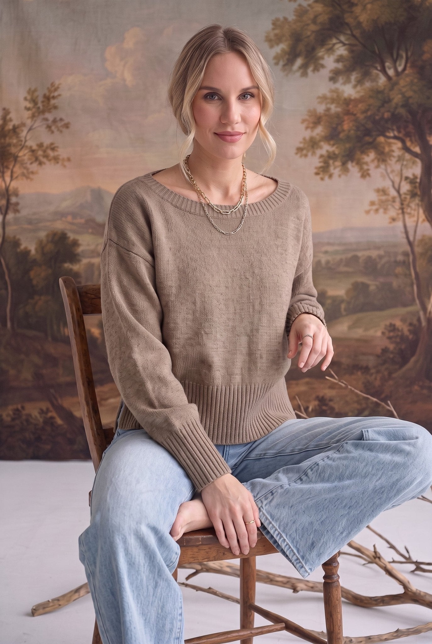 A woman wearing a graced taupe crew neck sweater with drop shoulders and ribbed hem, styled with light wash jeans.