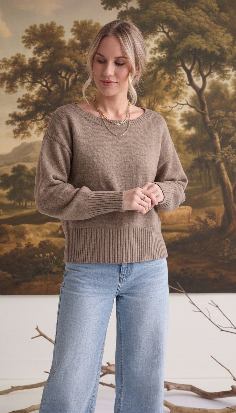 Woman wearing a graced taupe crew neck sweater with drop shoulders and wide ribbed hem paired with light wash jeans.