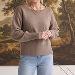 Woman wearing a graced taupe crew neck sweater with drop shoulders and wide ribbed hem paired with light wash jeans.