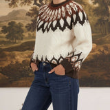 graced Fair Isle cable knit sweater in cream and brown worn by a woman with blue jeans against a landscape painting