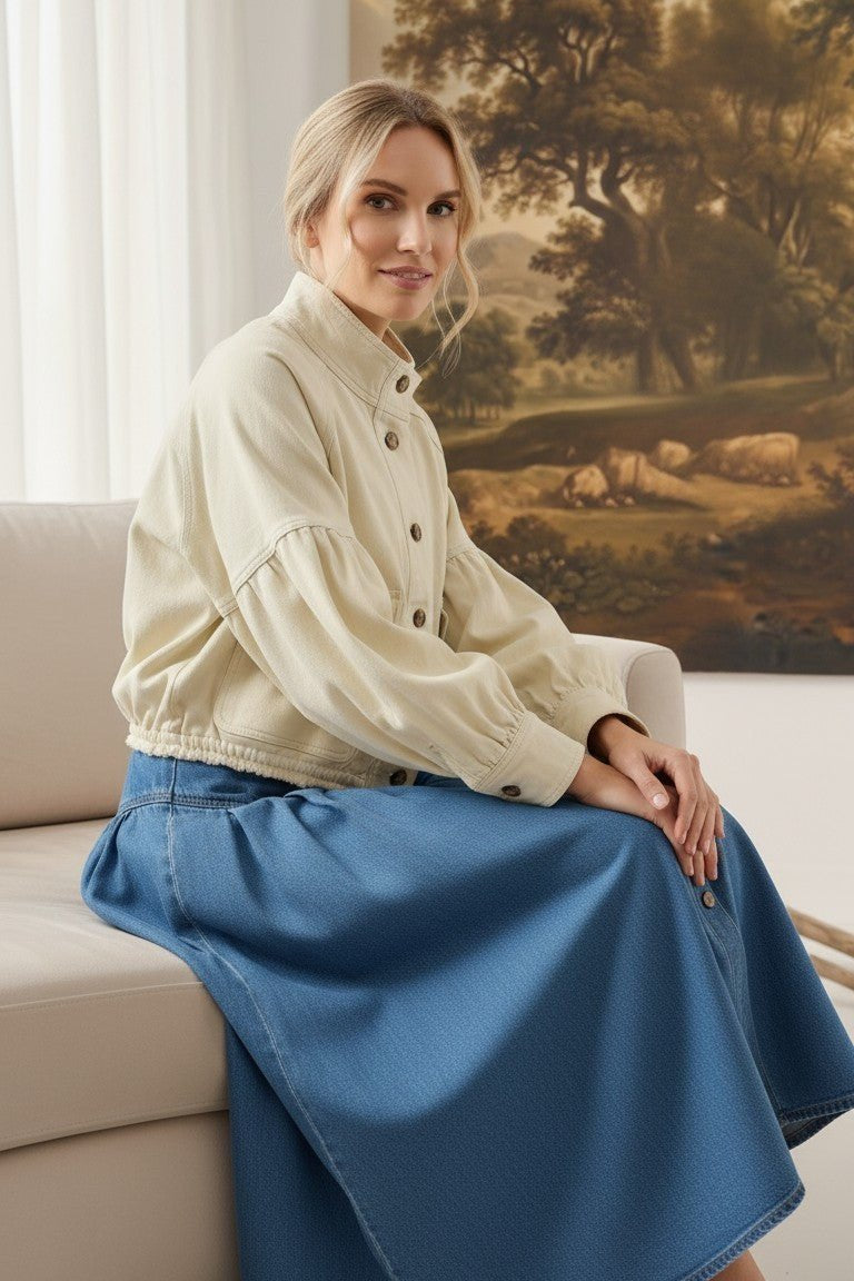 graced cream cotton balloon sleeve jacket worn by a woman sitting on a sofa with a blue denim skirt