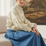 graced cream cotton balloon sleeve jacket worn by a woman sitting on a sofa with a blue denim skirt
