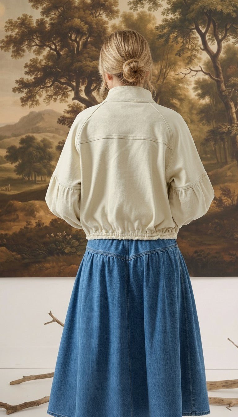 Back view of a model wearing the graced Jaden cream cotton balloon sleeve jacket with a blue denim skirt