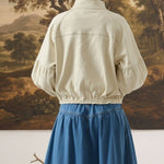 Back view of a model wearing the graced Jaden cream cotton balloon sleeve jacket with a blue denim skirt