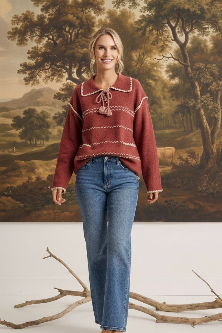 graced Jenna Whipstitch Sweater in rust red with contrast embroidery, collar, and tassel detail worn with blue jeans