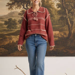 graced Jenna Whipstitch Sweater in rust red with contrast embroidery, collar, and tassel detail worn with blue jeans