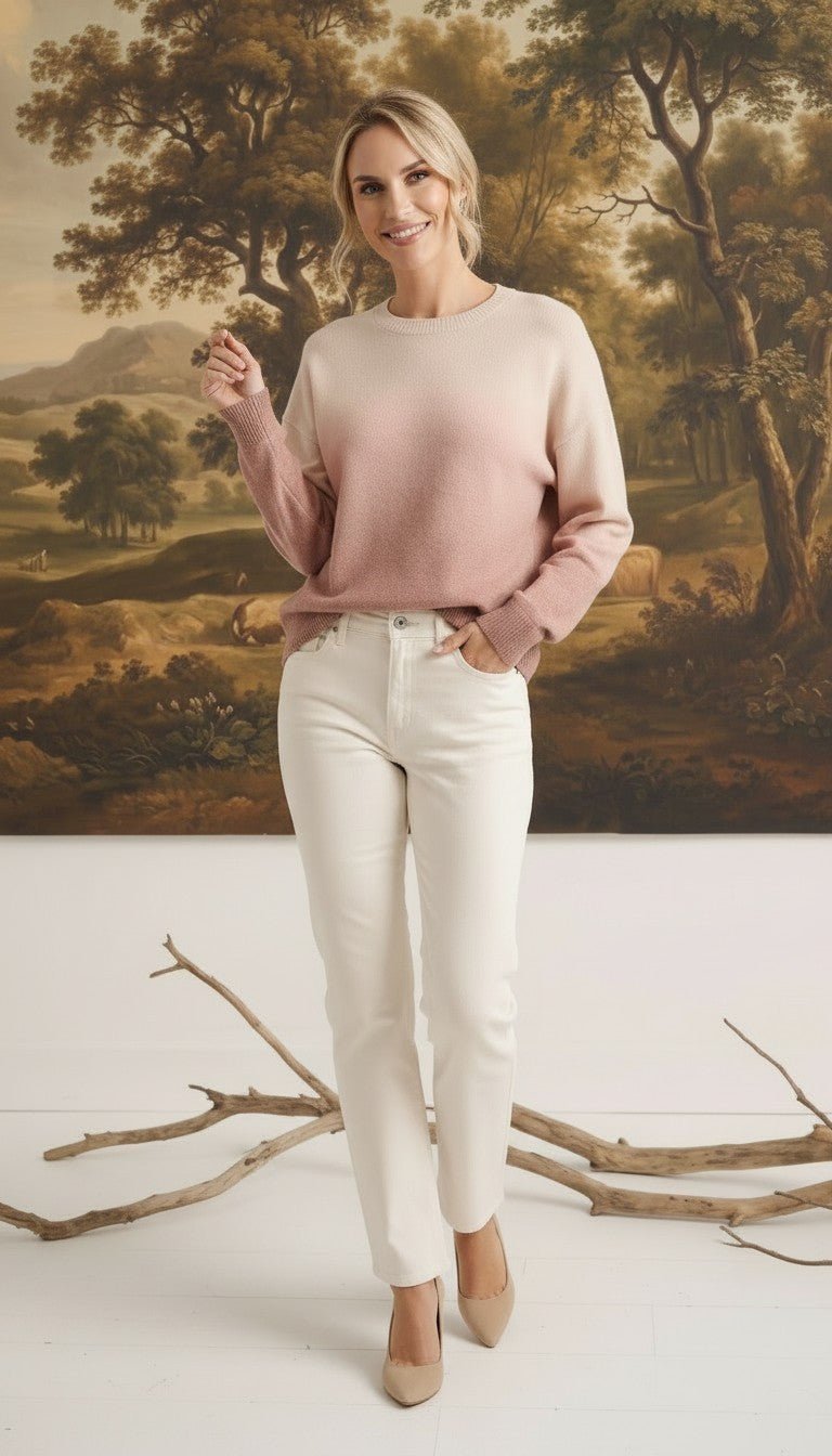 A model wearing a graced Joan gradient sweater in soft pink and cream tones with white jeans in a studio setting.