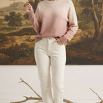 A model wearing a graced Joan gradient sweater in soft pink and cream tones with white jeans in a studio setting.