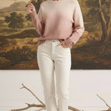 A model wearing a graced Joan gradient sweater in soft pink and cream tones with white jeans in a studio setting.