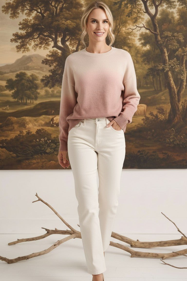 Model wearing a graced Joan gradient sweater in soft pink and cream tones with white jeans in a studio setting.