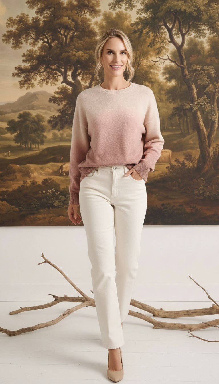 Model wearing a graced Joan gradient sweater in soft pink and cream tones with white jeans in a studio setting.