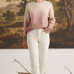 Model wearing a graced Joan gradient sweater in soft pink and cream tones with white jeans in a studio setting.