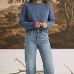 Model wearing a graced denim blue sailor sweater with textured knit detail, paired with light wash jeans and loafers.