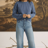 Model wearing a graced denim blue sailor sweater with textured knit detail, paired with light wash jeans and loafers.
