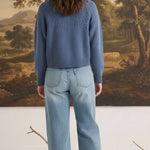 Back view of a woman wearing a graced Kaitlyn sailor sweater in denim blue with knit detailing paired with jeans