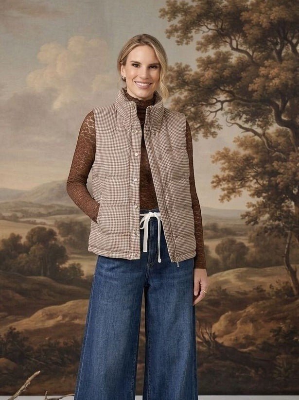 Model wearing a graced Karla gingham vest in tan over a brown lace top and wide-leg jeans against a landscape backdrop.