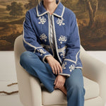 graced The Lea blue cotton jacket with white contrast floral embroidery, worn by a model sitting in a chair.