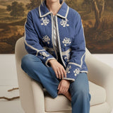 graced The Lea blue cotton jacket with white contrast floral embroidery, worn by a model sitting in a chair.