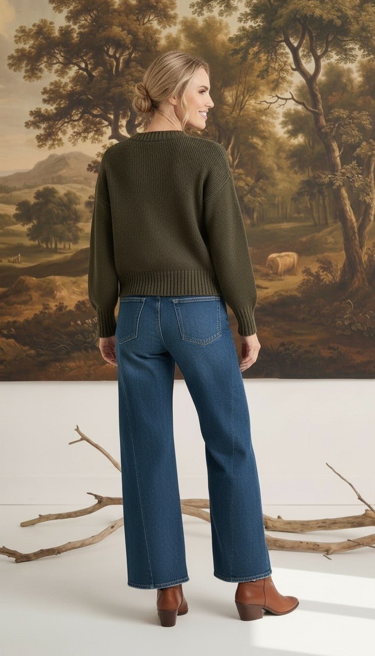 graced The Lily wide leg blue denim jeans worn by a model with an olive green sweater and brown ankle boots