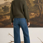 graced The Lily wide leg blue denim jeans worn by a model with an olive green sweater and brown ankle boots