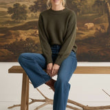 graced The Lily wide leg blue denim jeans paired with an olive green sweater and brown boots on a wooden bench