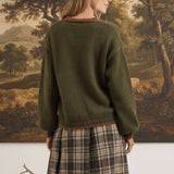 graced The Lola Pocket Detail Cardigan in olive green with brown trim, worn by a woman with a plaid skirt