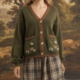 graced Lola cardigan in olive green with floral embroidery on pockets, worn over a plaid skirt by a blonde model
