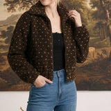 Model wearing a graced brown patterned fleece zip-up jacket with a high collar over a black top and blue jeans.