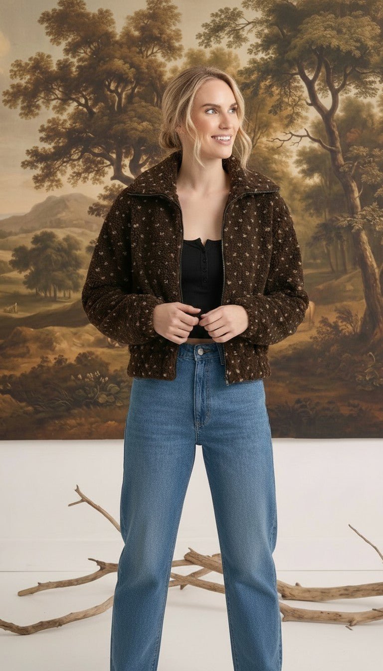 Model wearing a graced brown patterned fleece jacket with a zip-up collar and long sleeves over a black top.