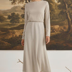 graced model wearing a beige wool-blend midi skirt and long-sleeve top in a studio with a landscape painting backdrop