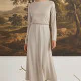 graced model wearing a beige wool-blend midi skirt and long-sleeve top in a studio with a landscape painting backdrop