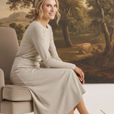graced Margo wool midi skirt in beige worn by a smiling model sitting on a chair in a classic interior setting