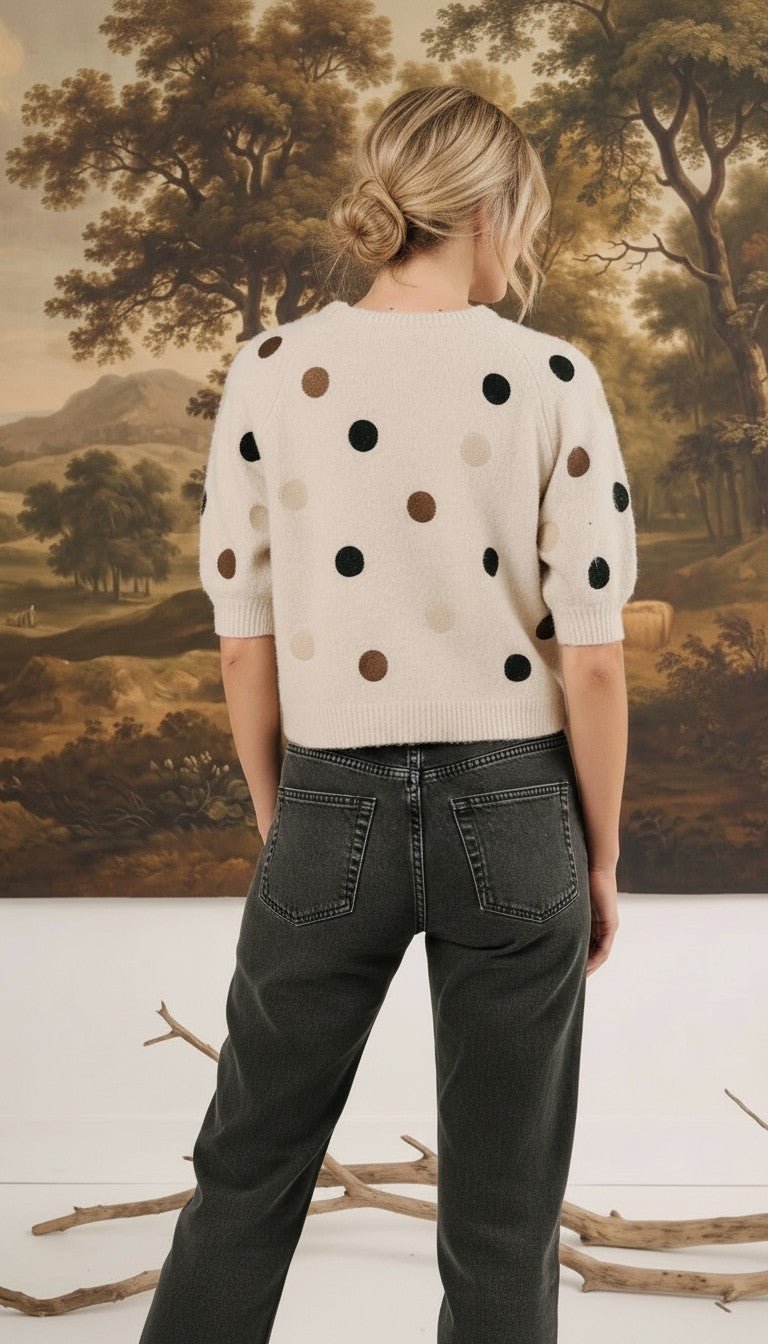 Back view of a woman wearing a graced cream knit top with multi-color polka dots and short sleeves with dark jeans.