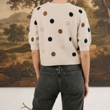 Back view of a woman wearing a graced cream knit top with multi-color polka dots and short sleeves with dark jeans.