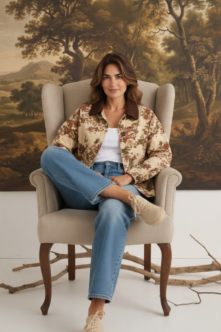 Model wearing graced The Morgan Floral Jacket with a brown collar, paired with blue jeans, sitting in an armchair.