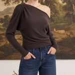 graced chocolate brown off-the-shoulder top with long sleeves and asymmetrical neckline worn with blue jeans