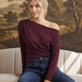 graced winetasting off the shoulder top with long sleeves worn by a woman sitting on a sofa