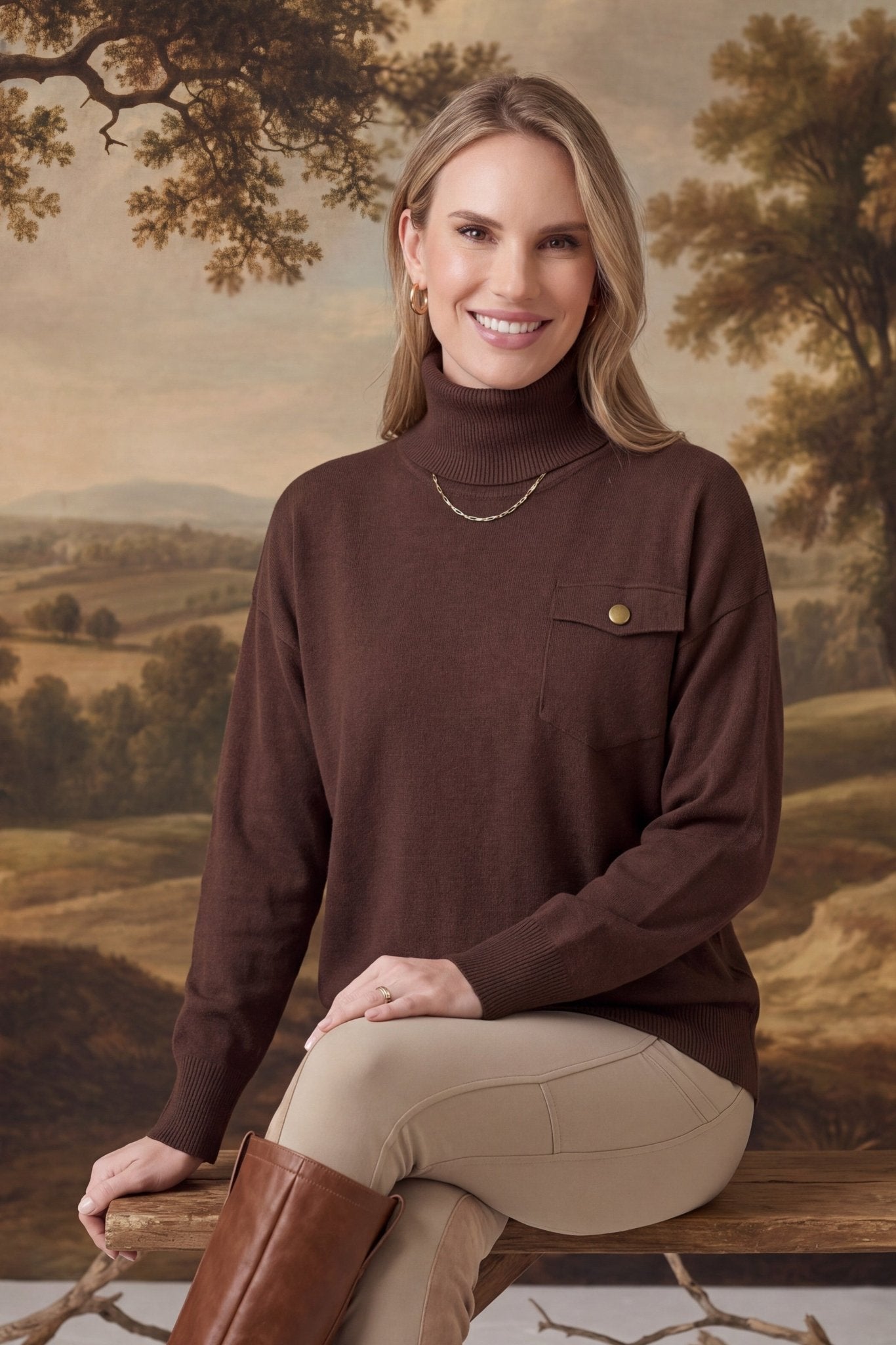 graced Remy brown turtleneck sweater with a single chest pocket, worn by a smiling woman in a rustic landscape setting