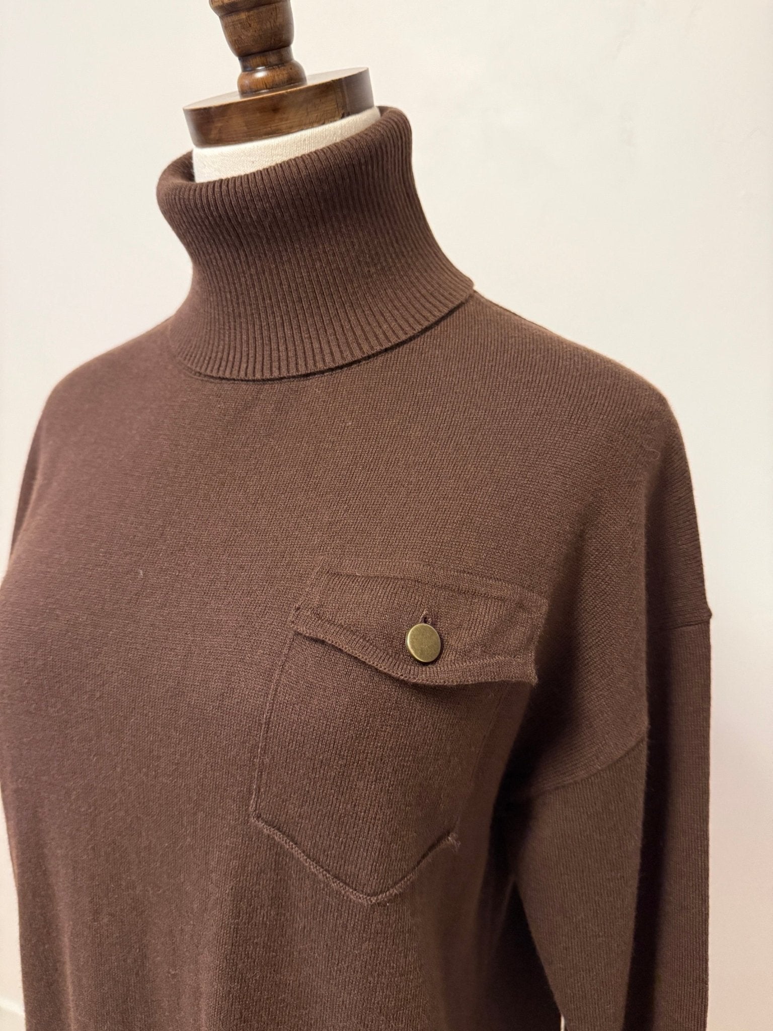 graced brown turtleneck sweater featuring a single chest pocket with a metal button on a mannequin